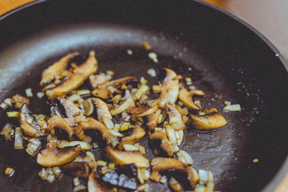 Close-up of sliced mushrooms and onions sautéing in a skillet, showcasing cooking detail.