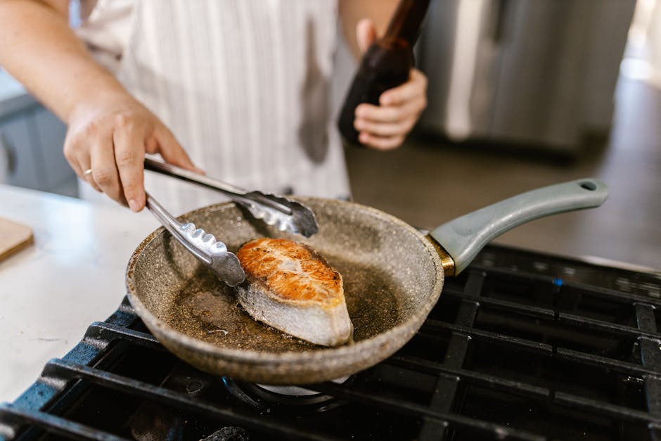 A close-up shot of a salmon steak being grilled in a non-stick pan in a kitchen setting. Perfect for cooking enthusiasts.