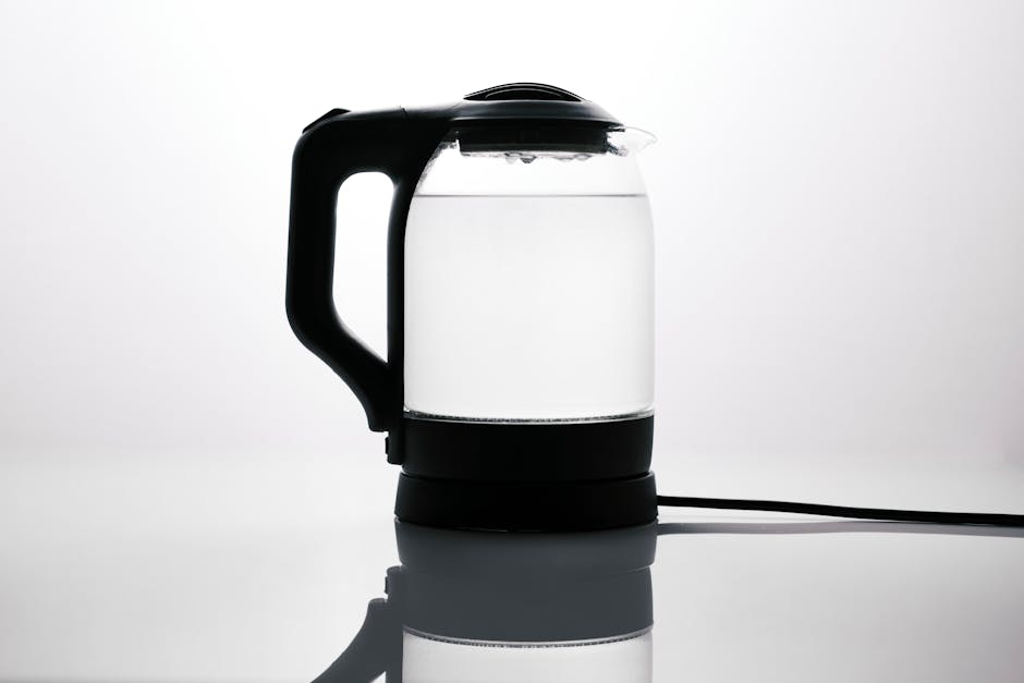 Sleek glass electric kettle with water, reflecting on a glossy surface, ideal for modern kitchens.