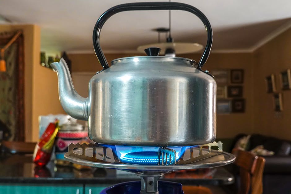 Close-up of a stainless steel kettle heating on a gas stove in a cozy kitchen setting.