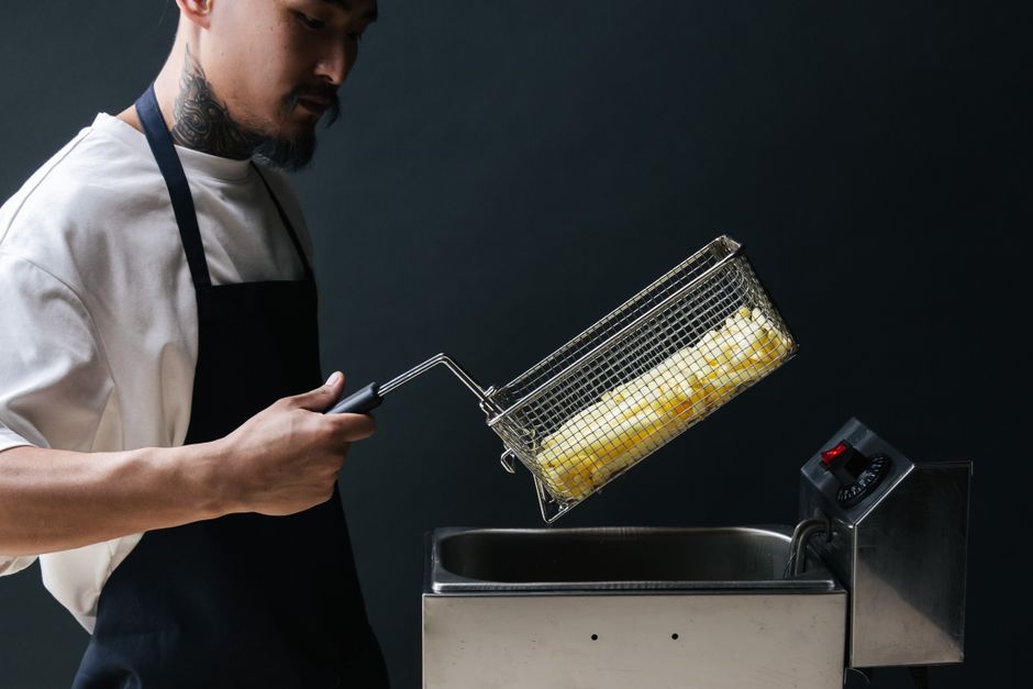 A chef uses a deep fryer to cook french fries. Indoor cooking scene.