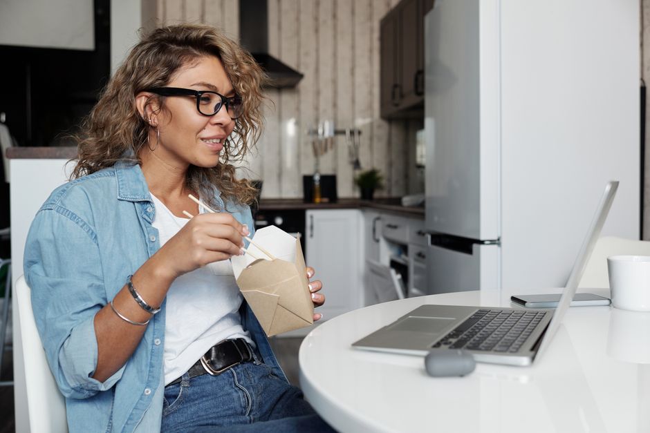 Woman eating lunch while attending a video call from her home kitchen.